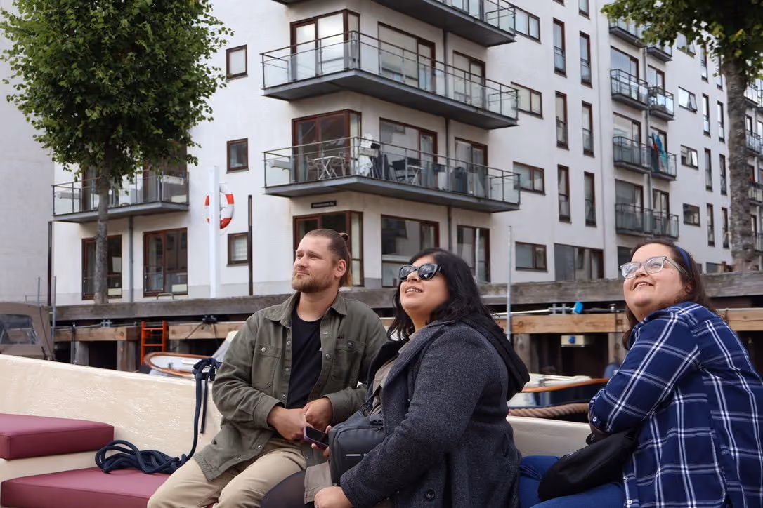 Three guests on a canal boat looking up at waterfront apartment buildings